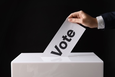 Photo of Woman putting her vote into ballot box on black background, closeup
