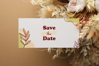 Photo of Beautiful card with Save the Date phrase and dry flowers on beige background, top view