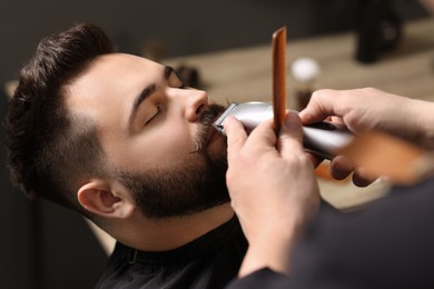 Photo of Professional barber trimming client's mustache in barbershop, closeup