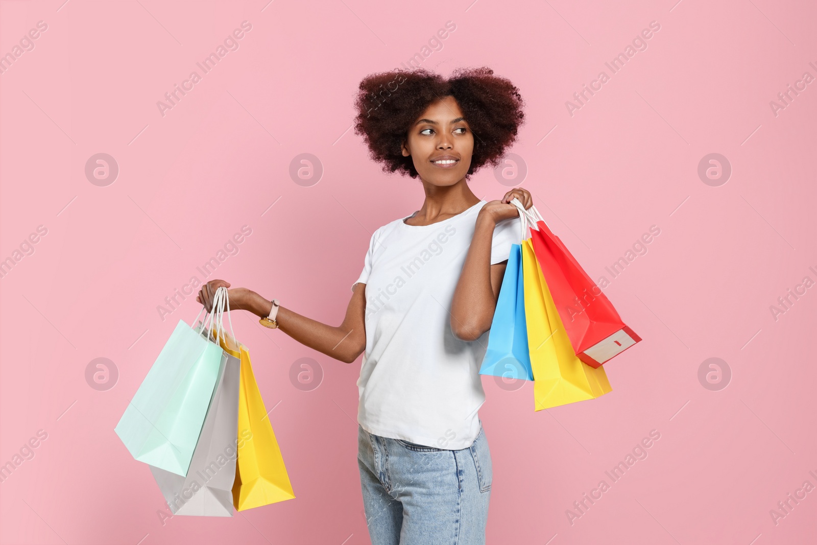 Photo of Happy African American woman with shopping bags on pink background