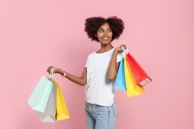 Happy African American woman with shopping bags on pink background