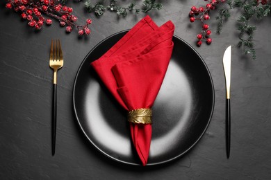 Photo of Plate with red fabric napkin, decorative ring and cutlery on black table, flat lay