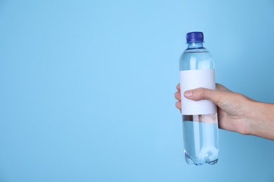 Woman holding plastic bottle with soda water on light blue background, closeup. Space for text