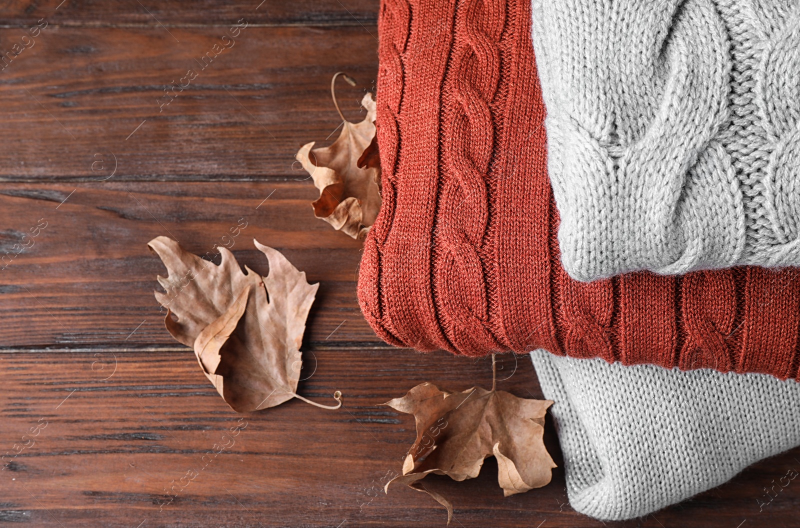 Image of Stack of folded warm sweaters and dry leaves on wooden background, closeup