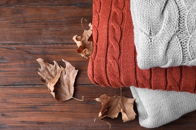 Stack of folded warm sweaters and dry leaves on wooden background, closeup