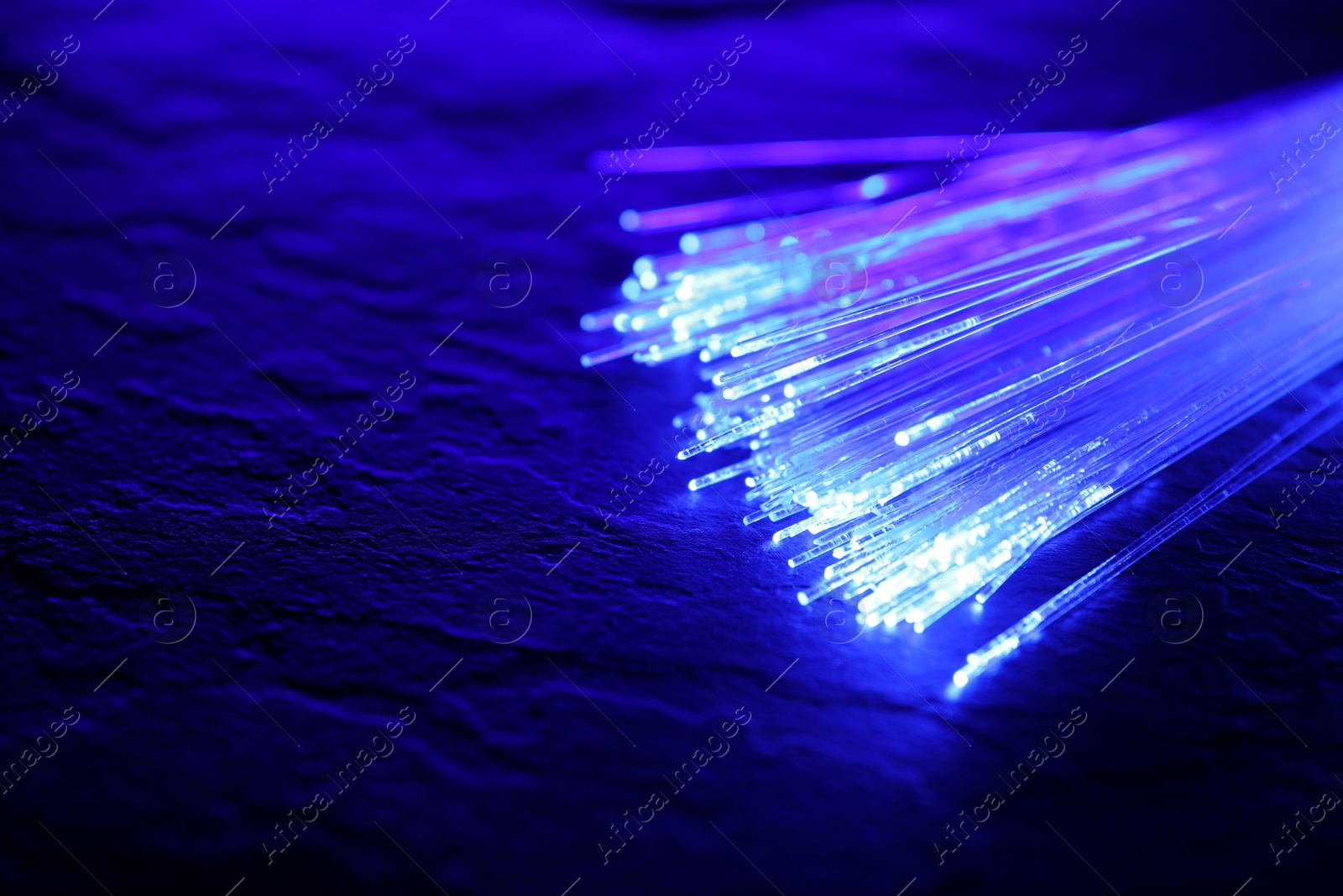 Photo of Optical fiber strands transmitting color light on textured background, closeup. Space for text