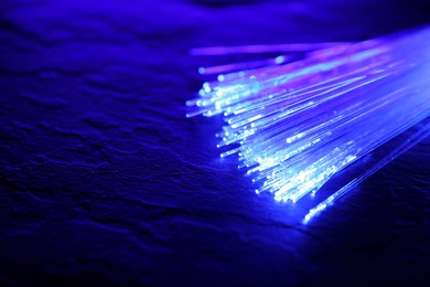 Optical fiber strands transmitting color light on textured background, closeup. Space for text