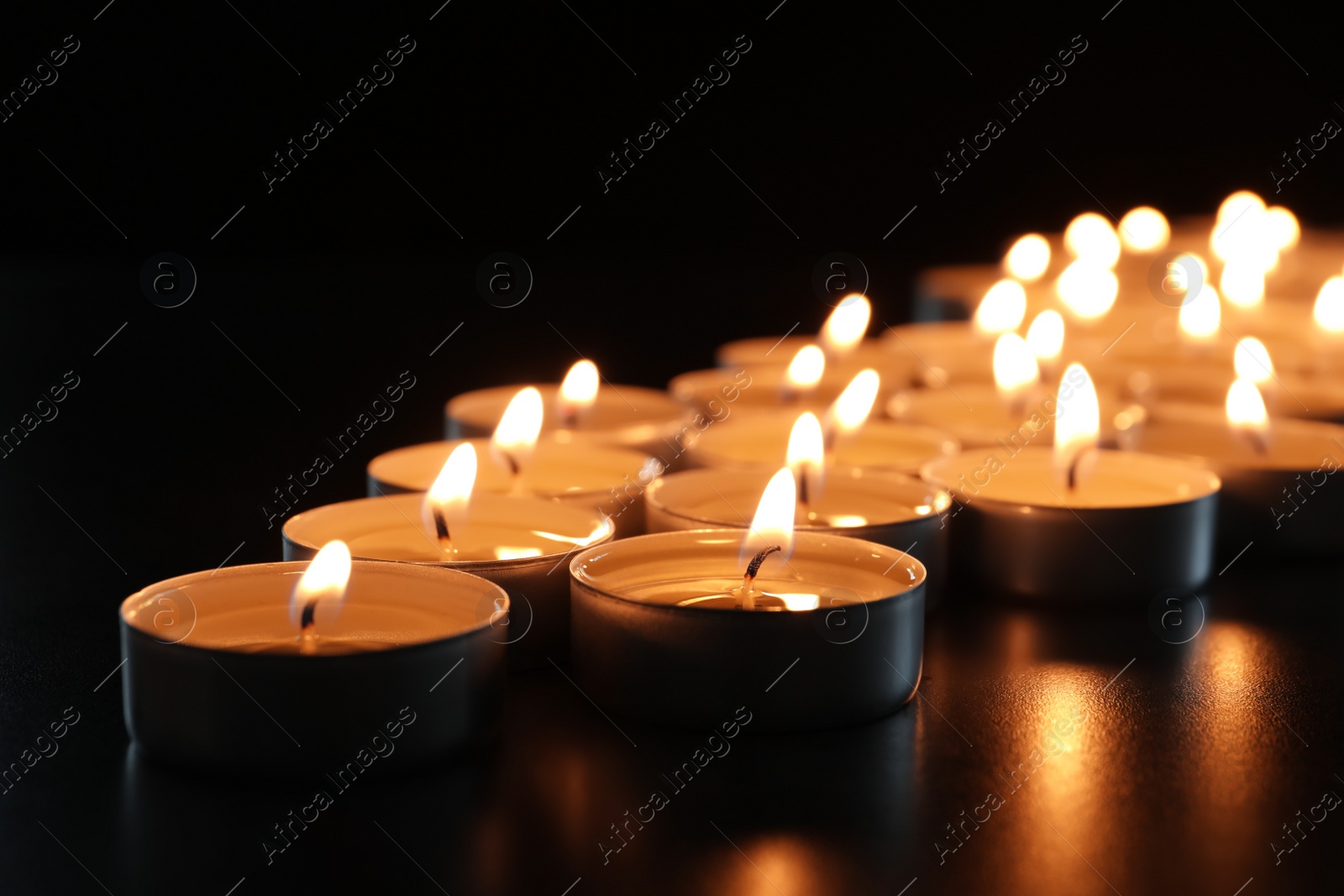 Photo of Wax candles burning on table in darkness, closeup