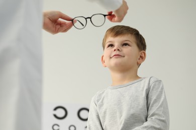 Photo of Vision testing. Ophthalmologist giving glasses to little boy indoors, low angle view