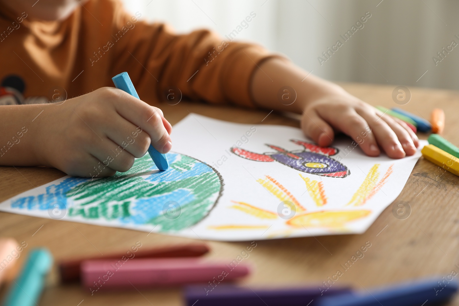 Photo of Little girl drawing picture with soft pastel at wooden table indoors, closeup. Child`s art