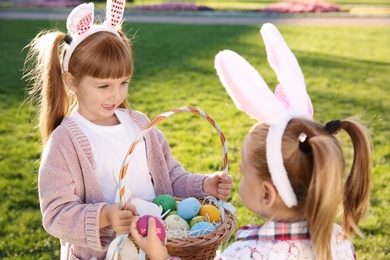 Cute little children with bunny ears and basket of Easter eggs in park