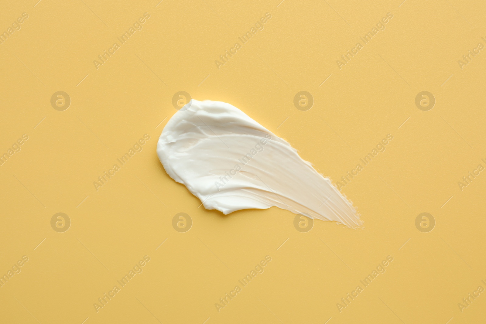 Photo of Sample of face cream on yellow background, top view