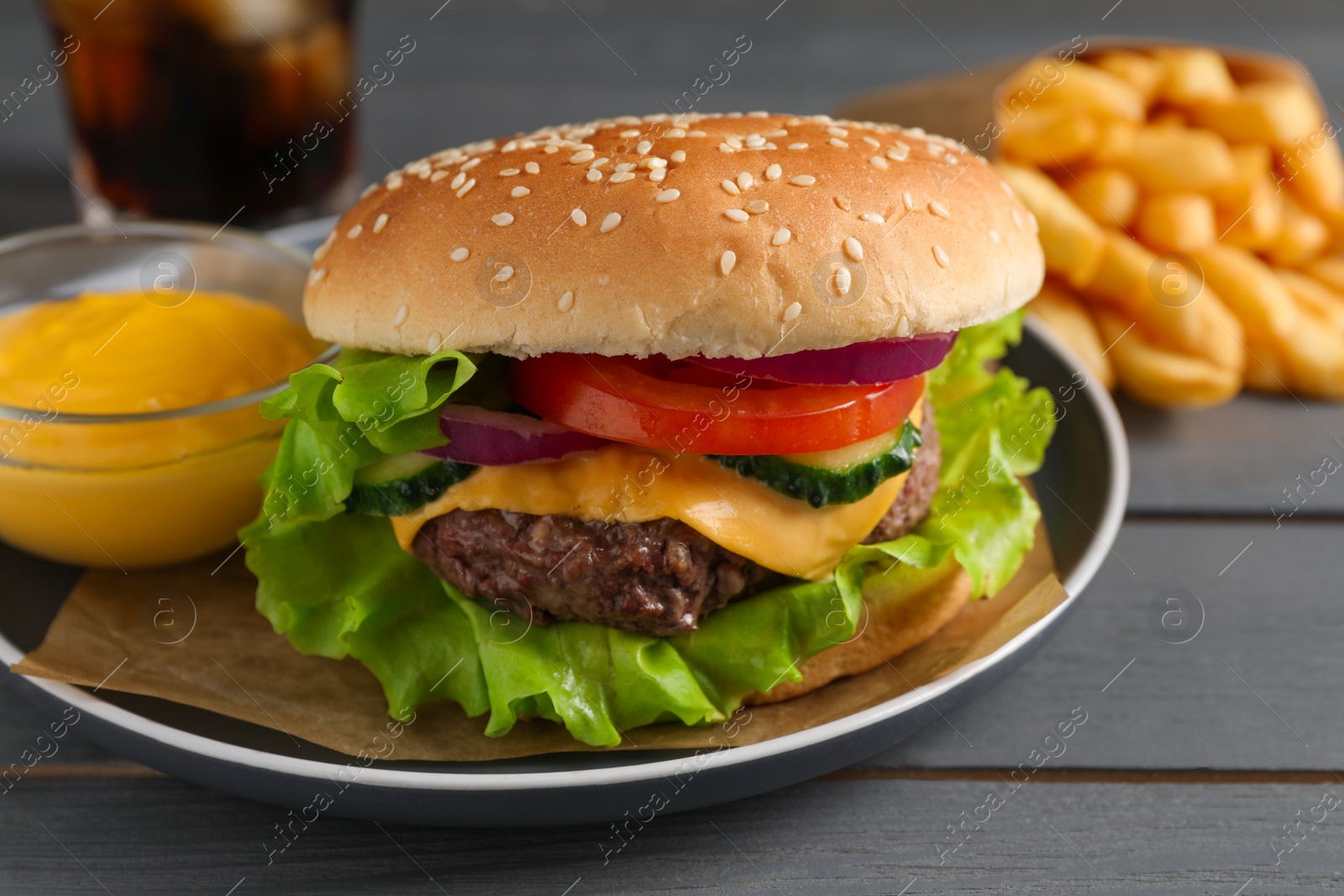 Photo of Delicious burger, soda drink and french fries served on grey wooden table, closeup