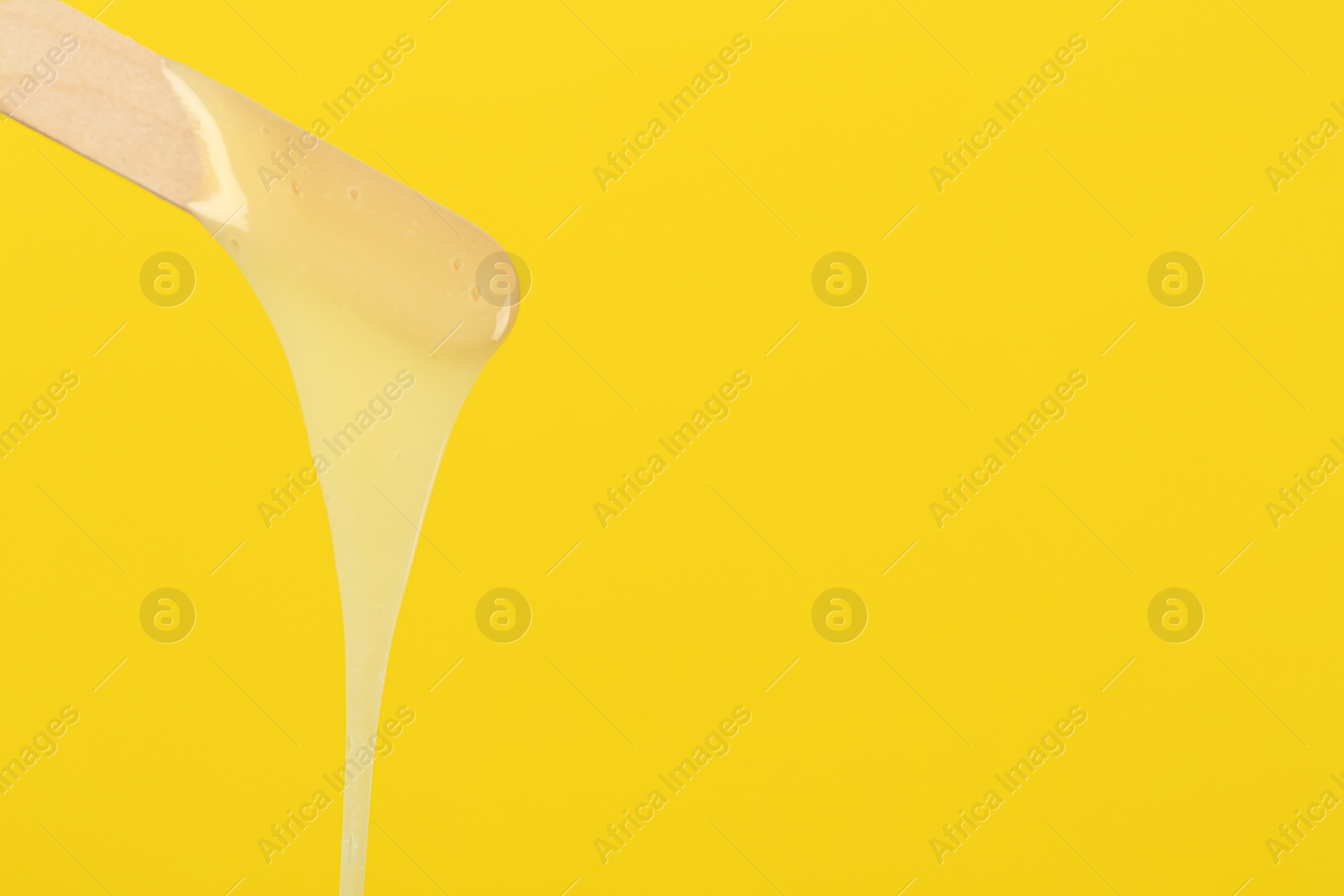 Photo of Wooden spatula with hot depilatory wax on yellow background. Space for text