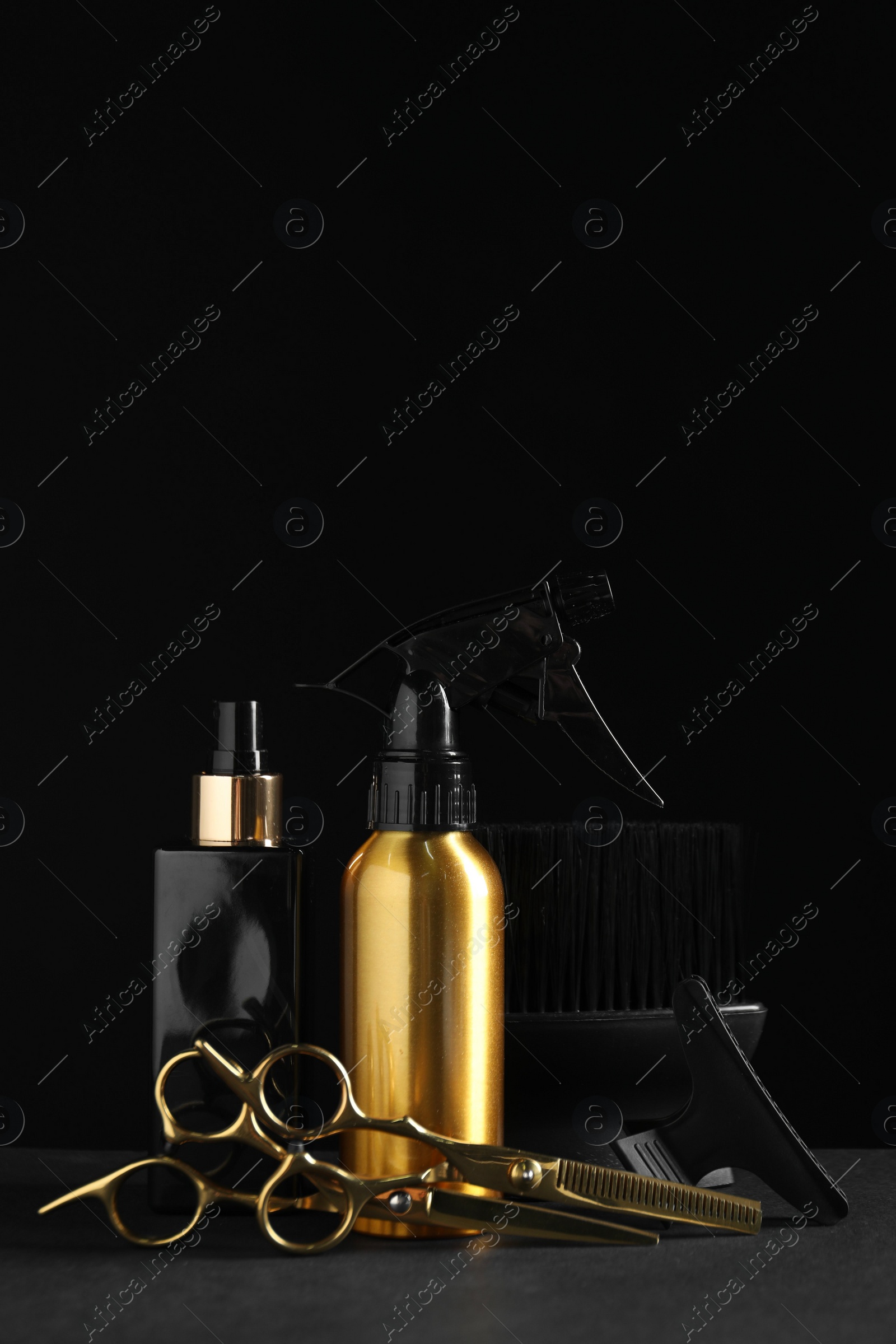 Photo of Different hairdresser tools on grey table against black background
