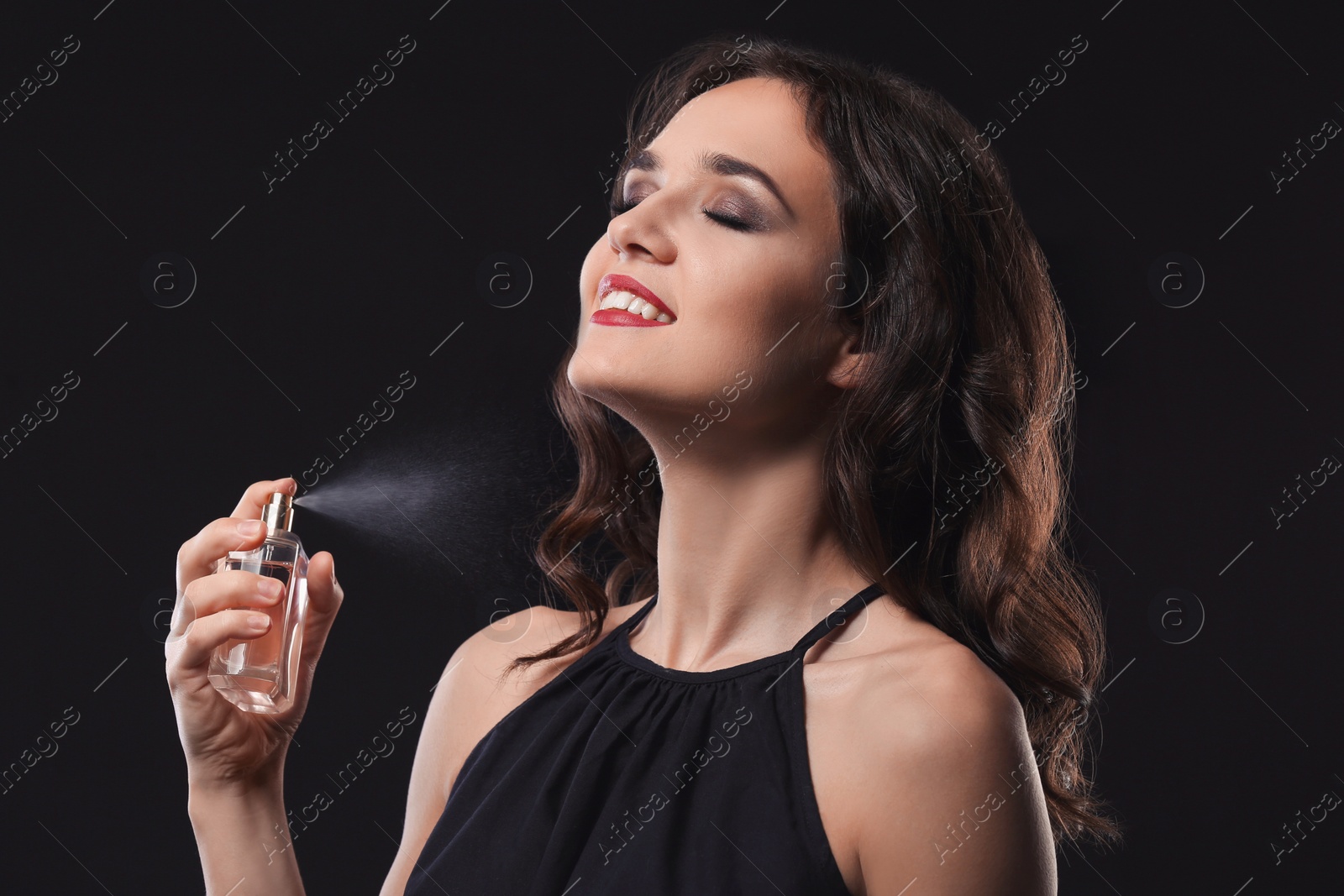 Photo of Beautiful young woman with bottle of perfume on black background