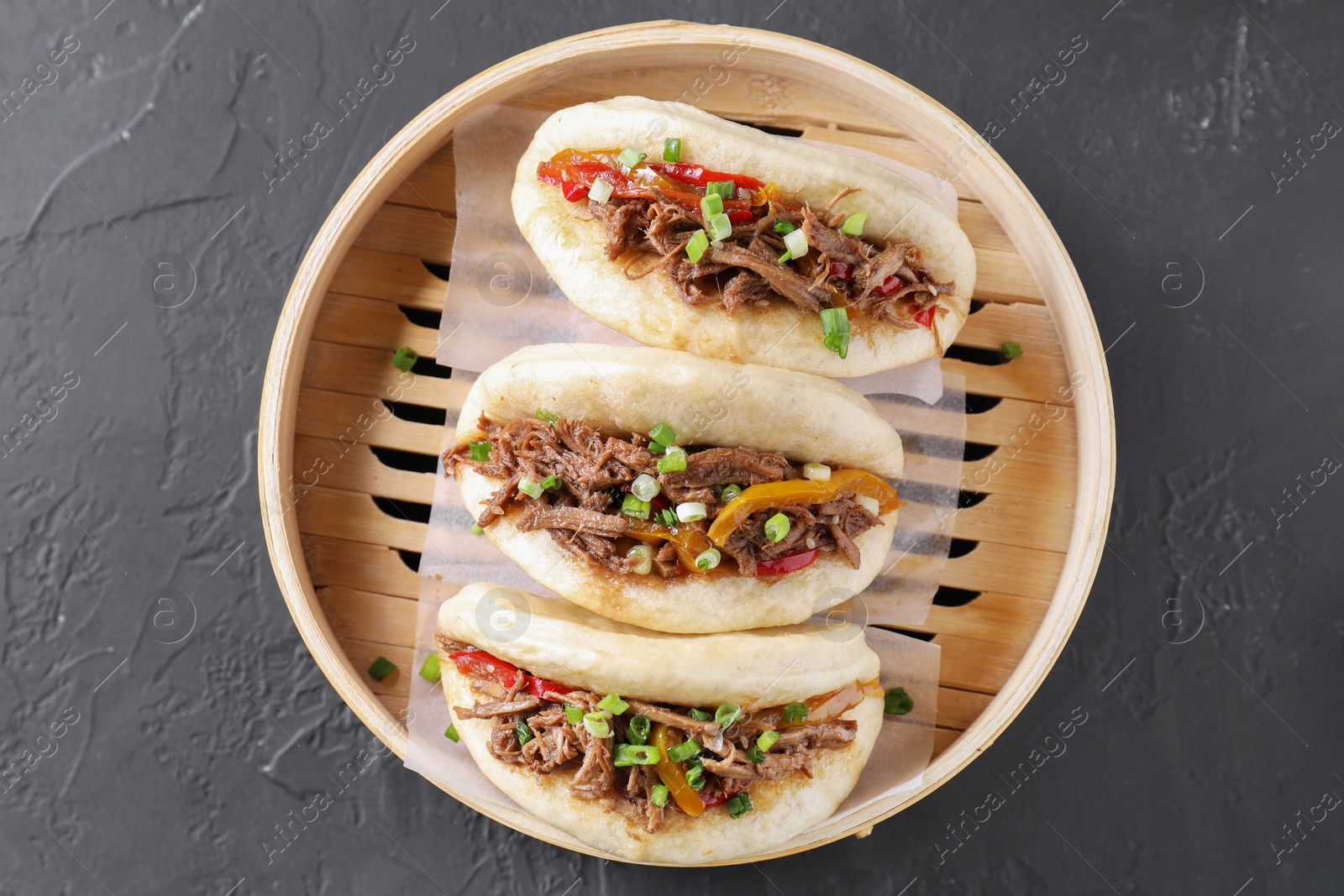 Photo of Delicious gua bao in bamboo steamer on black table, top view