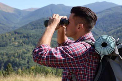 Photo of Tourist with backpack and sleeping pad looking through binoculars in mountains