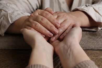 Photo of Woman holding hands with her mother at wooden table, closeup