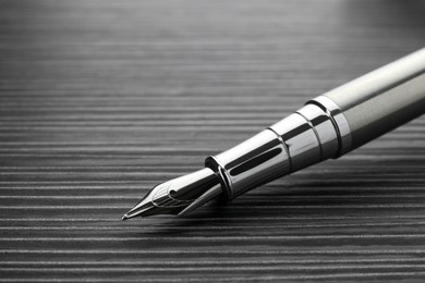 Photo of Stylish silver fountain pen on black wooden table, closeup