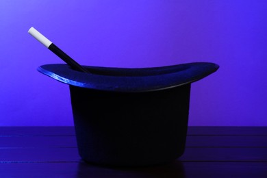 Black top hat and wand on wooden table. Magician equipment