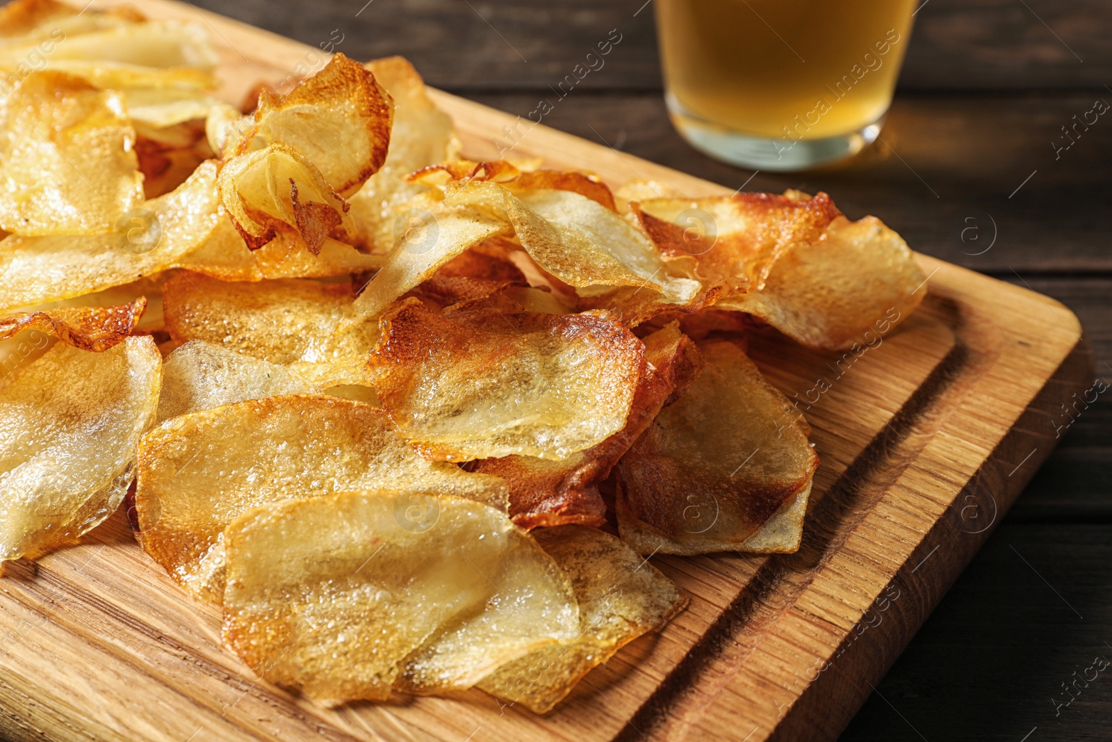 Photo of Wooden board with crispy potato chips on table, closeup