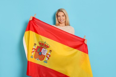 Photo of Woman with flag of Spain showing thumbs up on light blue background