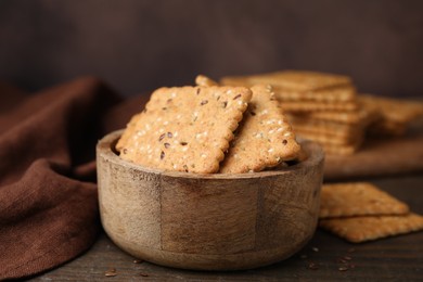 Photo of Cereal crackers with flax and sesame seeds in bowl on wooden table, closeup