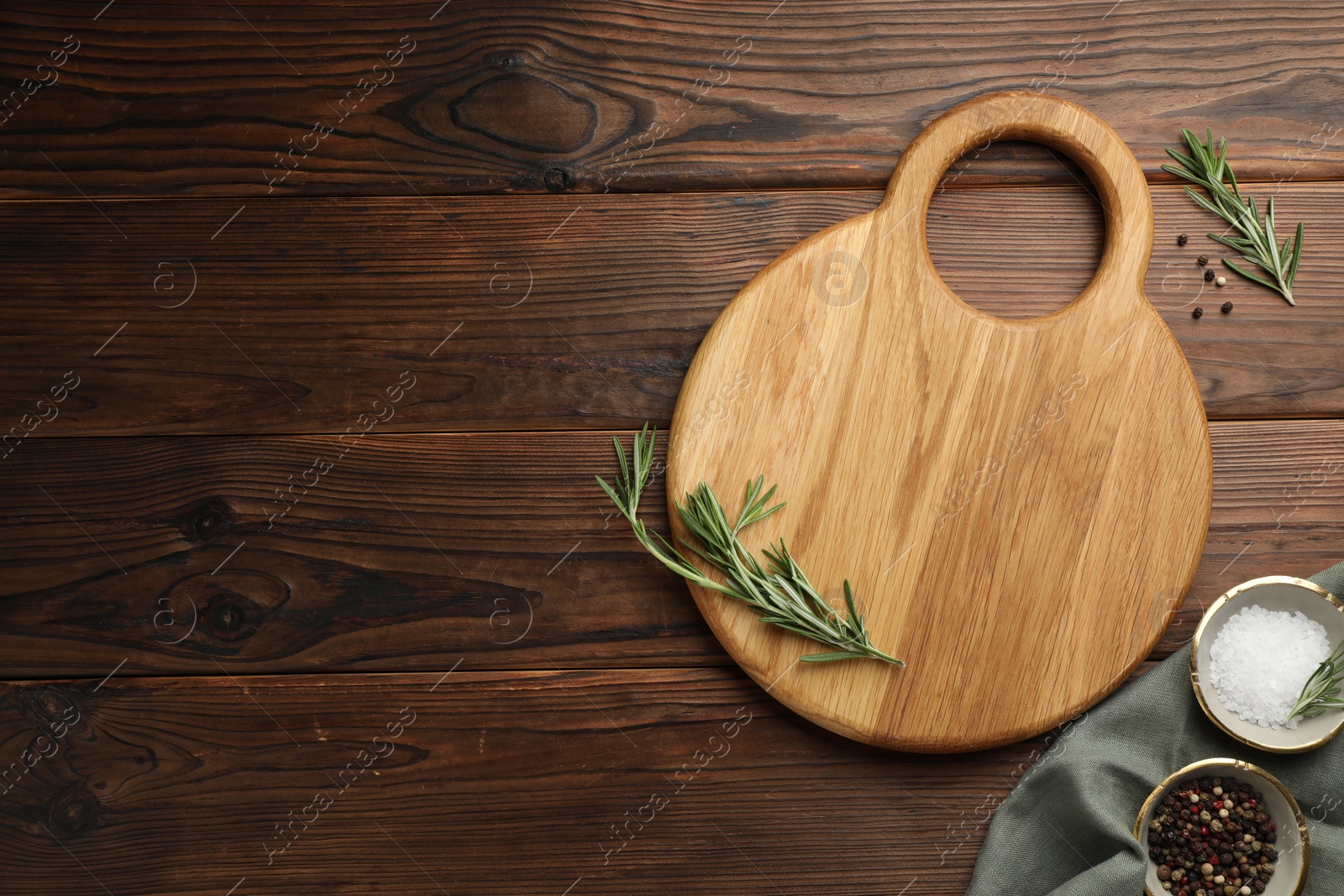 Photo of Cutting board, salt, pepper and rosemary on wooden table, flat lay. Space for text