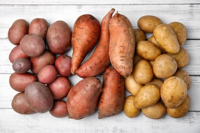 Photo of Different types of fresh potatoes on white wooden table, flat lay