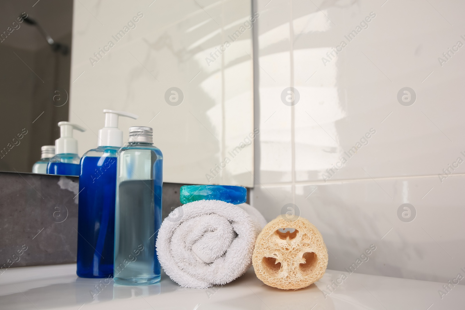 Photo of Loofah sponge, rolled towel and cosmetic products on sink in bathroom, space for text