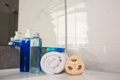 Photo of Loofah sponge, rolled towel and cosmetic products on sink in bathroom, space for text