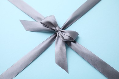 Photo of Grey satin ribbon with bow on light blue background, closeup
