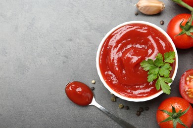 Photo of Delicious tomato ketchup in bowl, spices and products on grey textured table, flat lay. Space for text