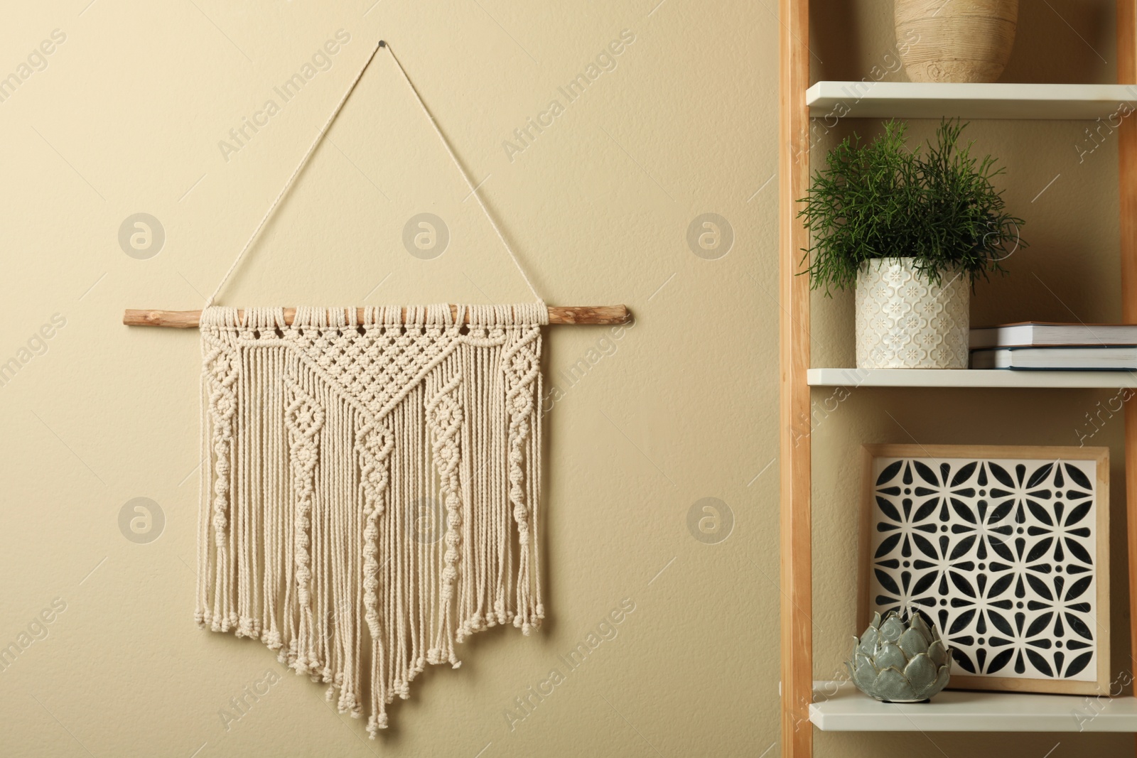 Photo of Beautiful macrame hanging on beige wall in room. Decorative element