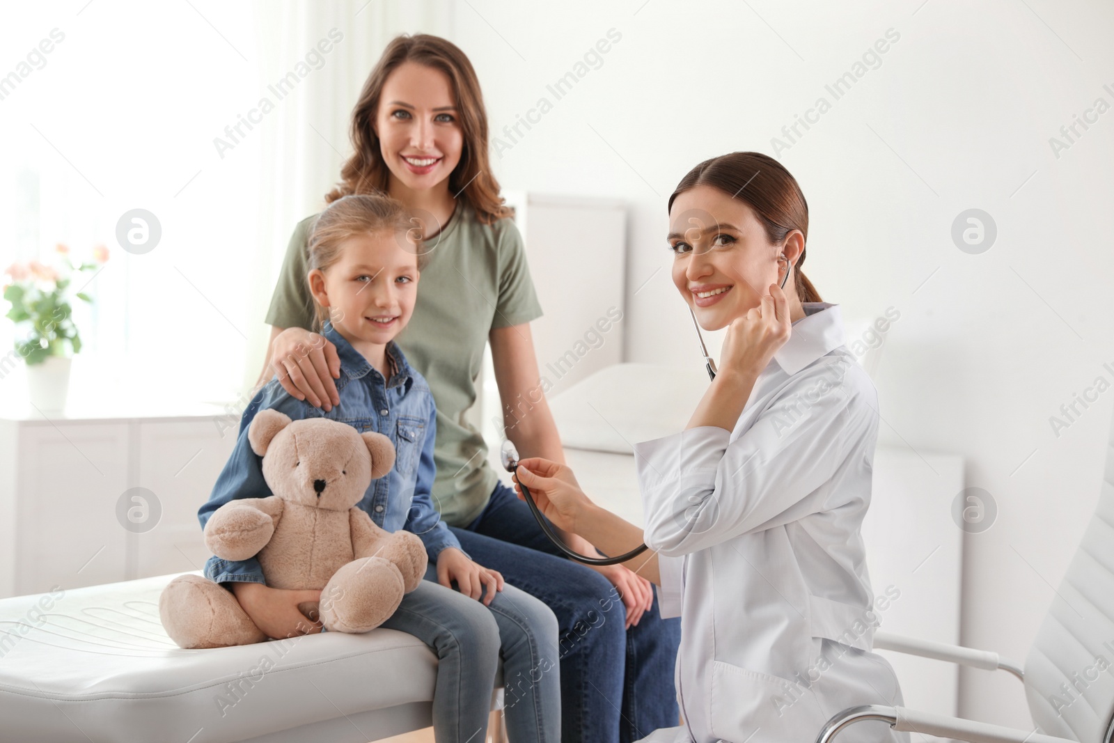 Photo of Mother and daughter visiting pediatrician. Doctor examining little patient with stethoscope in hospital