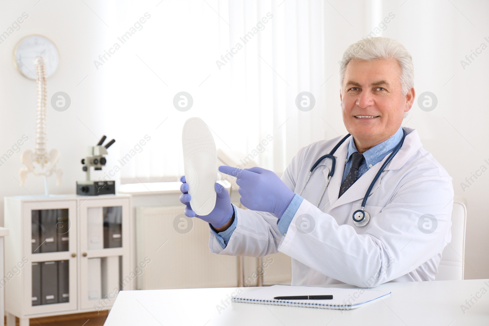 Photo of Senior male orthopedist showing insole in clinic