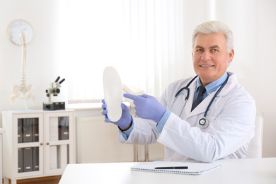 Senior male orthopedist showing insole in clinic