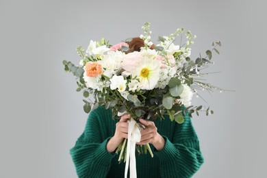 Photo of Woman covering her face with bouquet of beautiful flowers on grey background