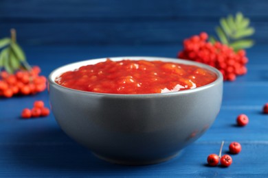 Photo of Delicious rowan jam in ceramic bowl on blue wooden  table, closeup