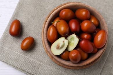 Fresh Ziziphus jujuba fruits with wooden bowl and napkin on table, flat lay