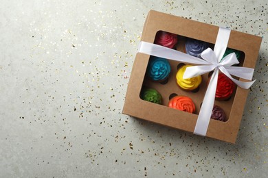 Photo of Box with delicious colorful cupcakes and confetti on light grey table, flat lay. Space for text