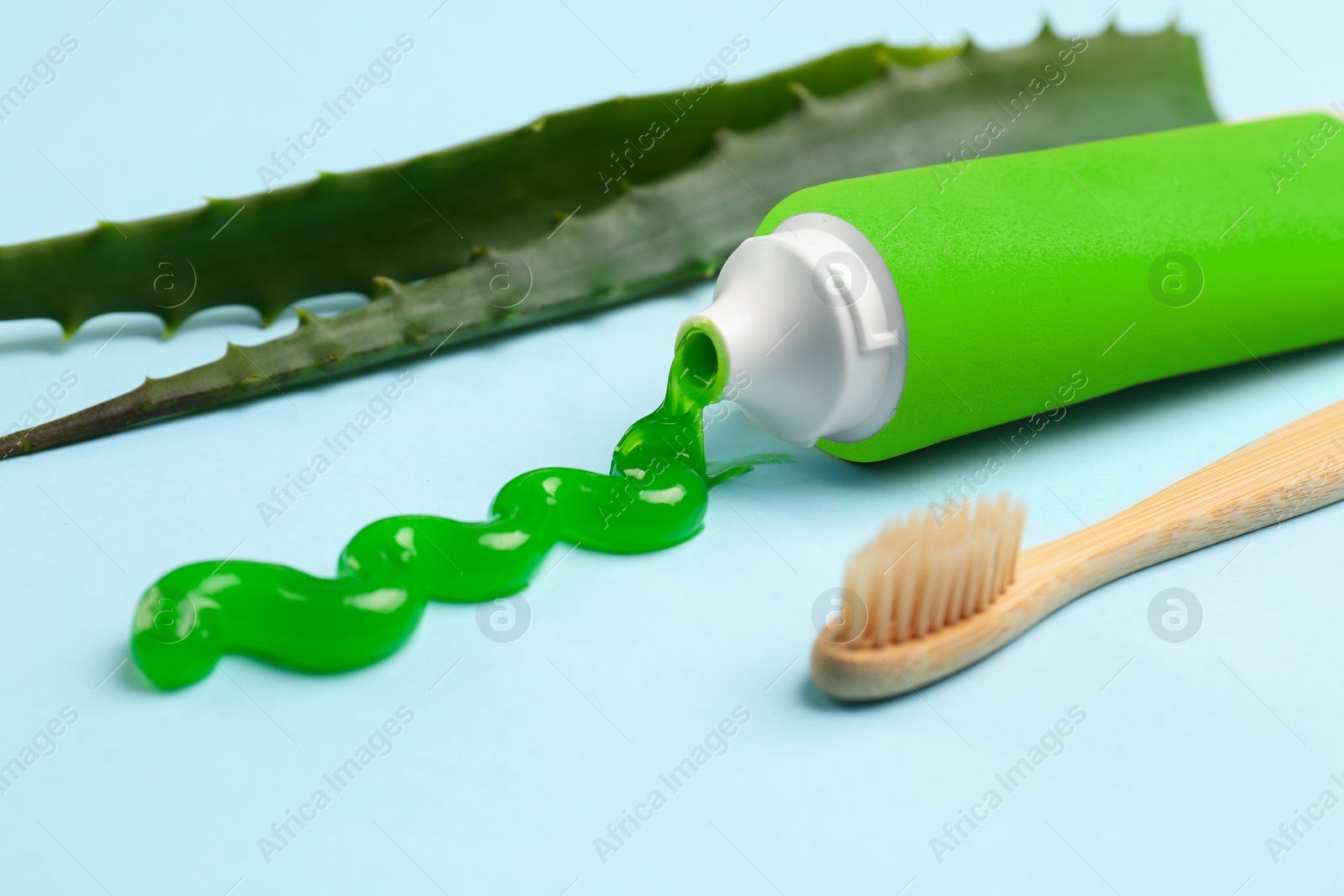 Photo of Tube of toothpaste, toothbrush and fresh aloe on light blue background, closeup