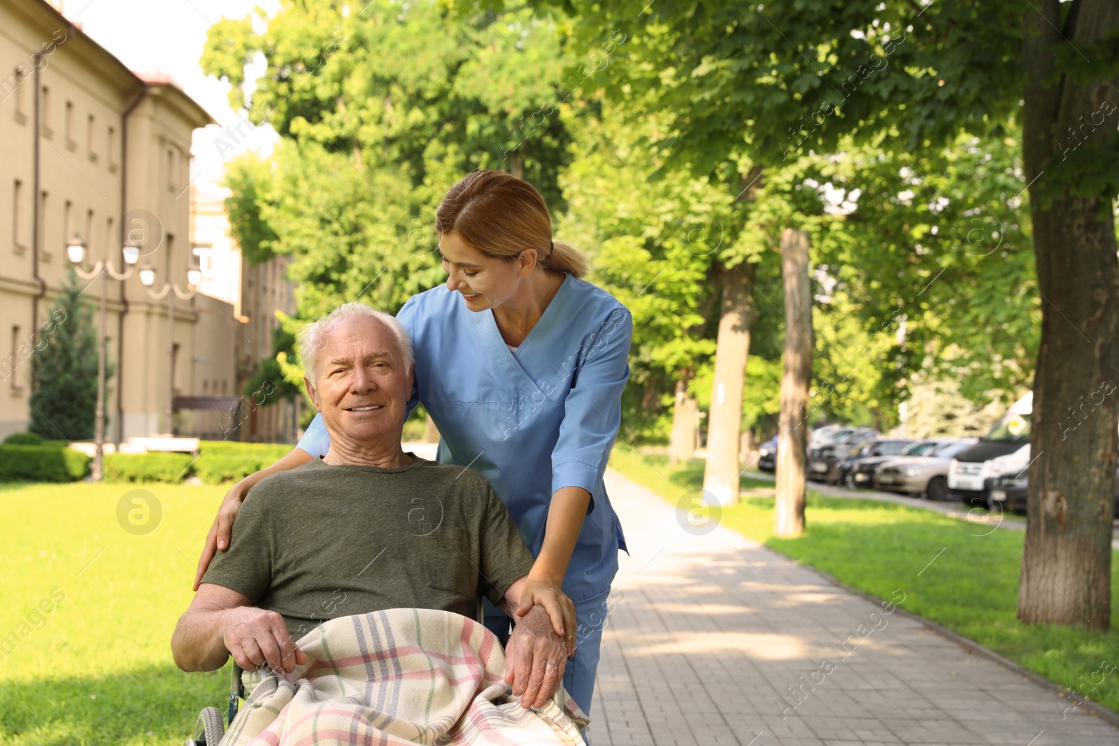 Photo of Happy nurse assisting elderly man in wheelchair at park