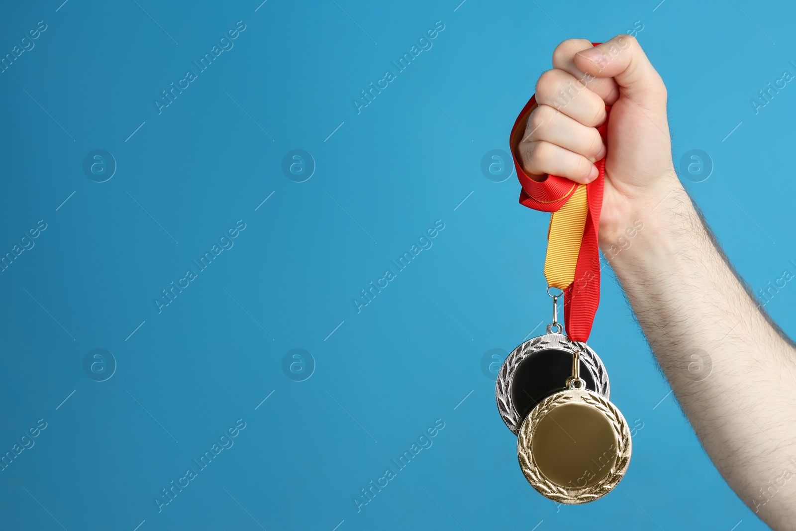 Photo of Man holding medals on blue background, closeup. Space for design