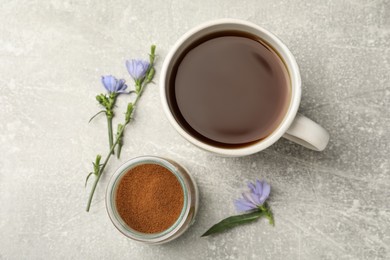 Photo of Cup of delicious chicory drink, powder and flowers on light grey table, flat lay