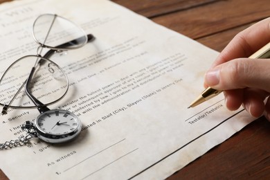 Photo of Woman signing Last Will and Testament at wooden table, closeup