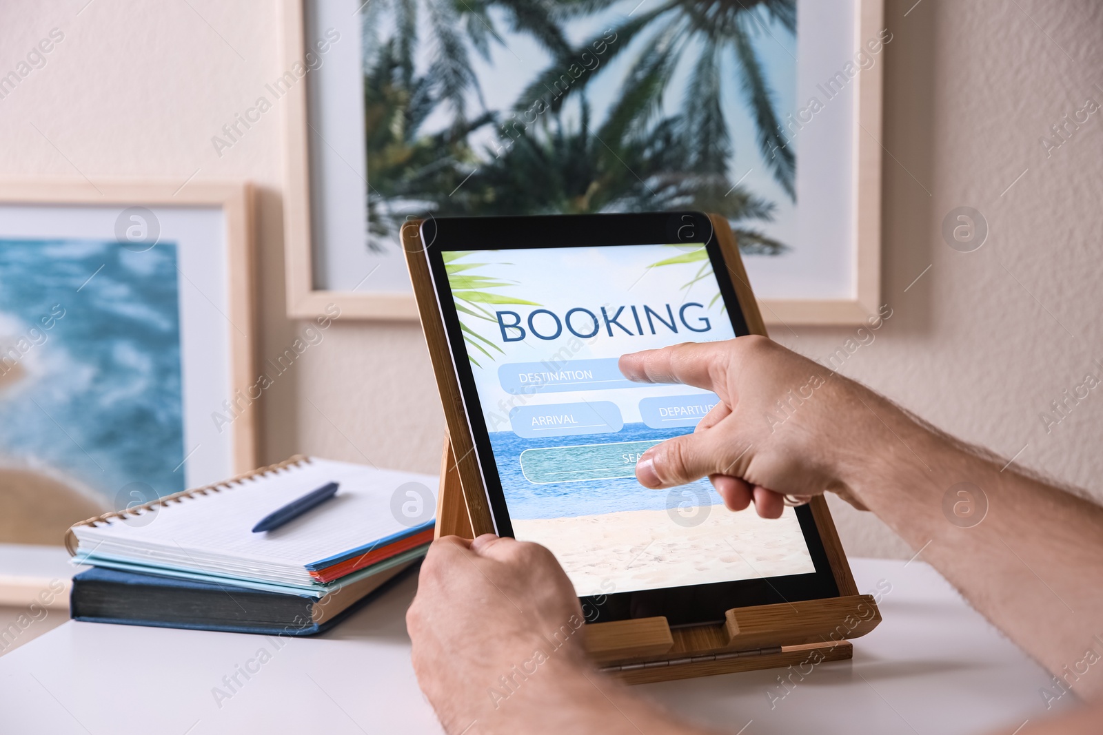 Photo of Man booking tickets online on tablet at white table, closeup. Travel agency concept