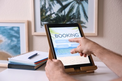 Man booking tickets online on tablet at white table, closeup. Travel agency concept