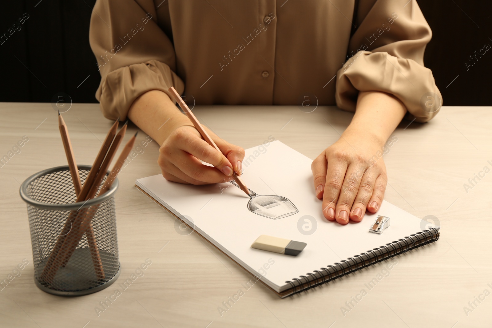 Photo of Woman drawing glass of wine with graphite pencil at light wooden table, closeup